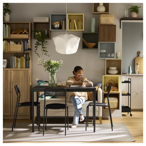 Girl with teddy bear at study table under floral light, surrounded by bookshelves.