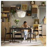 Girl with teddy bear at study table under floral light, surrounded by bookshelves.