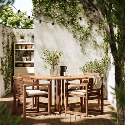 Outdoor dining set with wooden table and four beige-cushioned chairs under string lights.