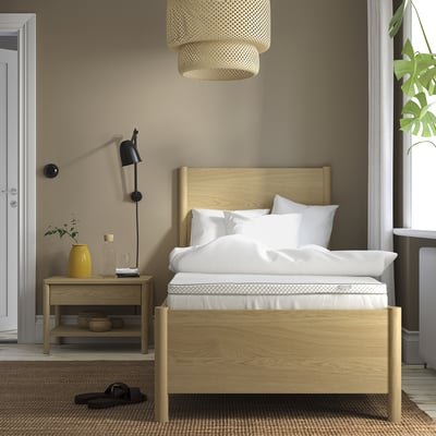 Minimalist bedroom with light wood bed, white bedding, bedside table with decor, pendant lamp, large window, and rug.