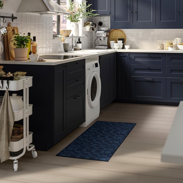 Modern kitchen with dark blue cabinets, white washing machine, blue diamond rug, and mobile cart.
