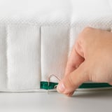 Person unlocking child-safe zipper on NATTSMYG mattress. The tool used is a paper clip, showcasing its safety feature.