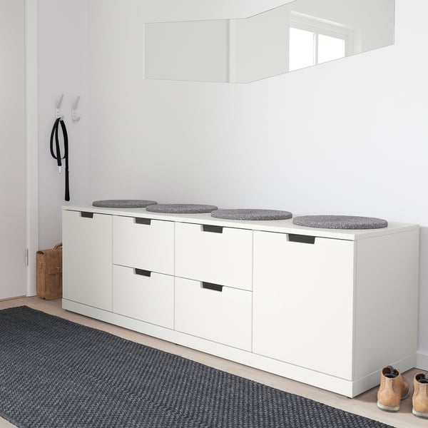 Minimalist white NORDLI chest with cushioned seats, holding four round gray stools, contrasting with a black-and-gray rug and a single tan boot.