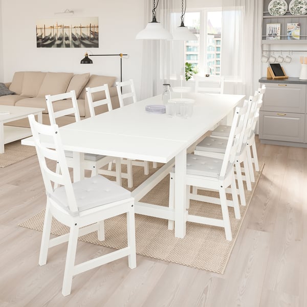 Bright dining room with white NORDVIKEN extendable table seating 8. Matching white chairs, big window, natural light, adjacent living space with sofa.