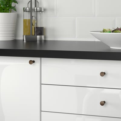 Modern kitchen cabinets, black countertop, white drawers with bronze handles, salad bowl.