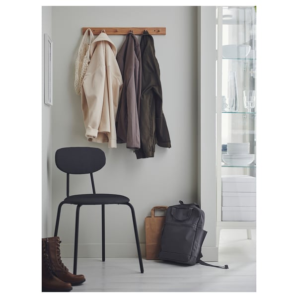 Modern entryway with an ÖSTANÖ chair in black, wooden coat hangers, backpack, boots, and glass shelving.