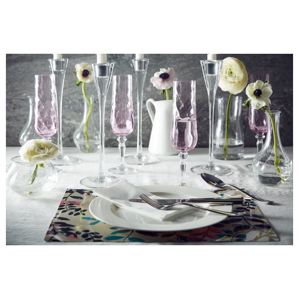 Elegant table setting with white OFANTLIGT dinnerware, clear glassware, and pink floral place mats. Single flowers in small vases.