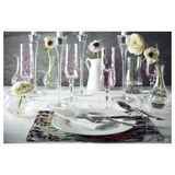 Elegant table setting with white OFANTLIGT dinnerware, clear glassware, and pink floral place mats. Single flowers in small vases.