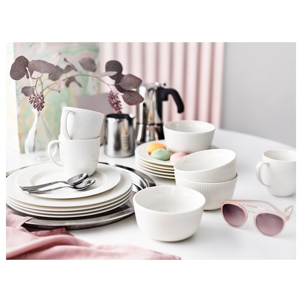 White porcelain dinnerware set with cups, bowls, and plates on a table with pink accents, featuring elegant vertical lines and a modern design.
