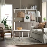 Modern living room with colorful rug, grey armchair, white coffee table, wooden side table, wicker lamp, and decorations.