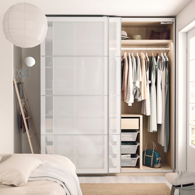 Modern bedroom with white PAX wardrobe, hanging clothes, shelves, and accessories.
