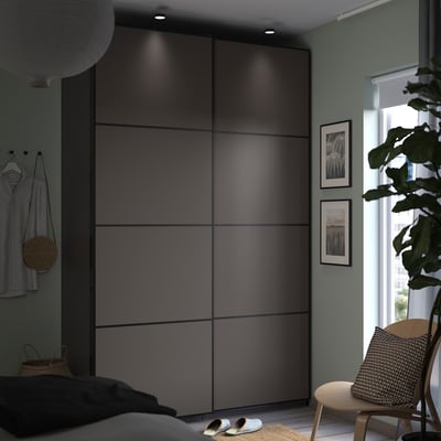 Modern minimalist bedroom with black PAX wardrobe, striped shirt, slippers, and potted plant by window.