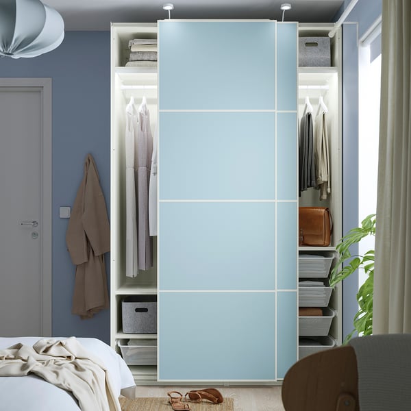A modern bedroom a blue PAX wardrobe with sliding doors, revealing organized clothes and accessories inside.