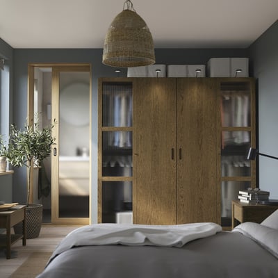 Modern bedroom with PAX wardrobe, grey bed, plant, and wicker pendant lamp.