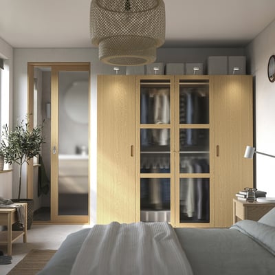 Modern bedroom with large PAX wardrobe, grey bed, plant, and pendant light. Wardrobe with glass doors and grey boxes.