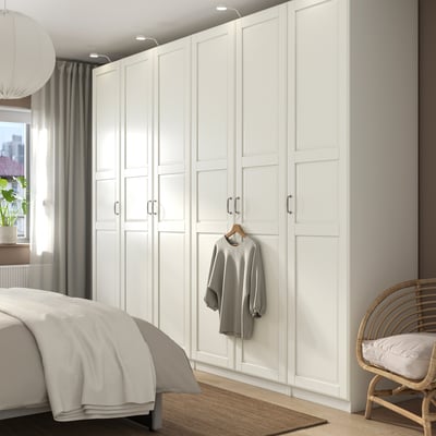 Modern white PAX wardrobe towering over bed, housing grey sweater, complementing minimalist bedroom decor.