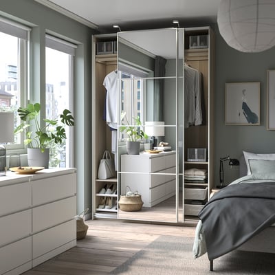 Modern bedroom with PAX wardrobe, white, wooden floor, green walls, plants, bed with gray linens, city view window.