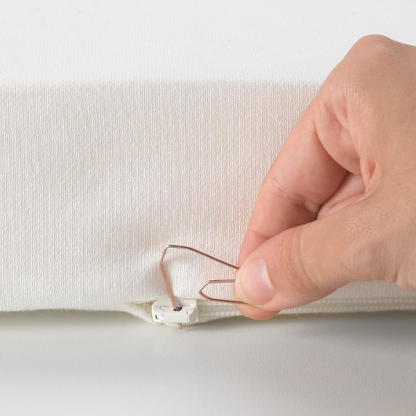 Hand using paper clip to open child-safe zipper on reversible mattress cover.