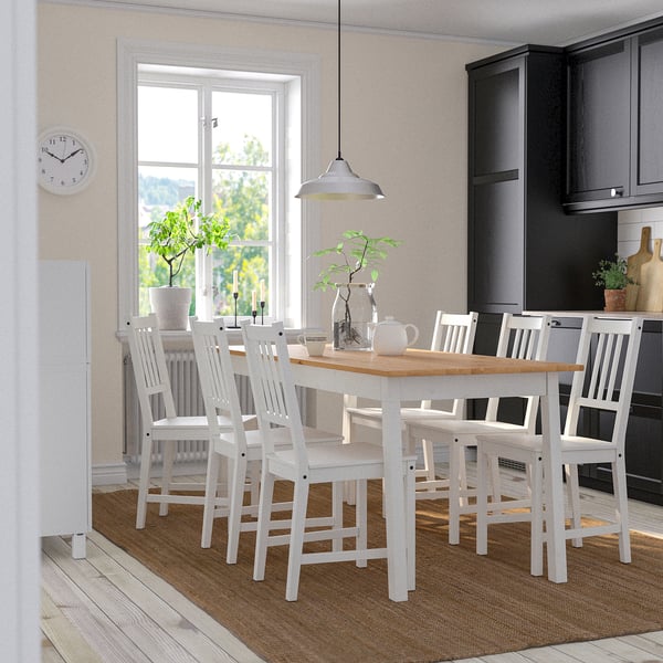 Cozy kitchen with white PINNTORP dining set. Six matching chairs, brown rug, dark cabinets, hanging light.