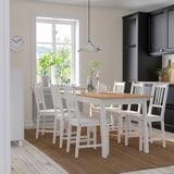 Cozy kitchen with white PINNTORP dining set. Six matching chairs, brown rug, dark cabinets, hanging light.