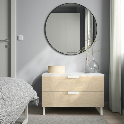 Minimalist bedroom: tall white bed, wooden PLATSA dresser, round mirror.