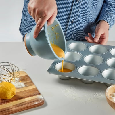 A kitchen scene with ingredients and tools for baking, including a bowl with a spout, whisk, spatula, and grater, ready for mixing and preparing food.