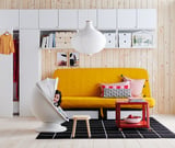 Yellow sofa, colorful pillows, modern room, white lamp, unique chair, striped shirt, black rug.