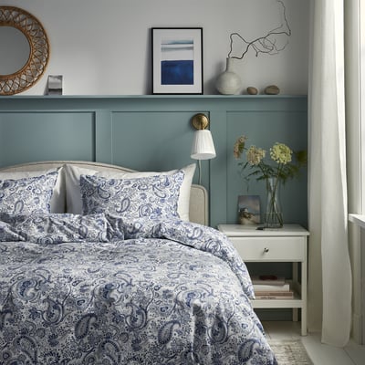Green headboard bed, blue paisley bedding, vase on nightstand, calm cozy room.