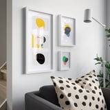 Modern room with white walls, colorful paintings, black armchair, cream pillow, tall lamp.