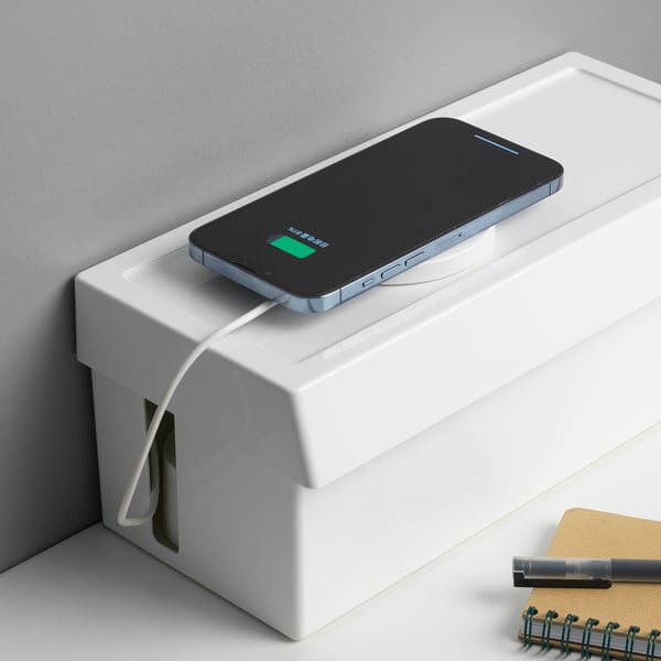 A smartphone charging on a box. The box organizes cables and hides connectors.