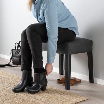 Person in blue shirt and boots on stool, bag nearby.