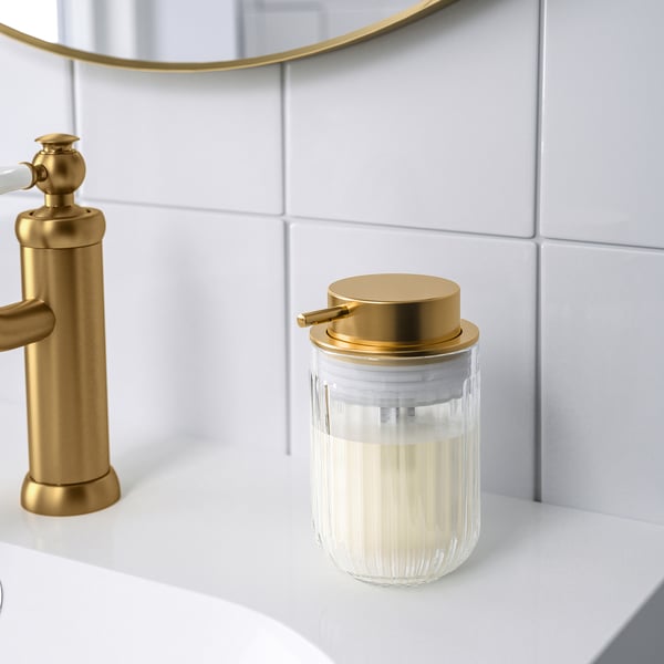 Gold soap dispenser on white counter next to gold faucet.