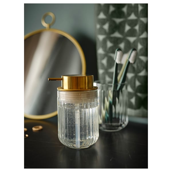 Silvtjarn soap dispenser, clear glass with gold pump, fluted design, sits on dark table with toothbrush holder and mirror.