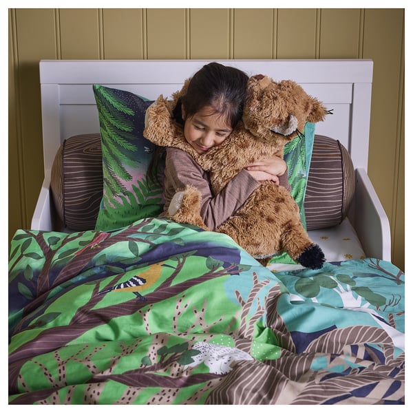 Child hugging large lynx plush toy on bed with green jungle-themed sheets.