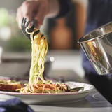 Chef serving cooked spaghetti with tongs.
