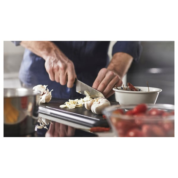 Chef chops garlic on SLÄTROCKA cutlery-board. Steel blade, white cloves, blue apron. Kitchen setup.