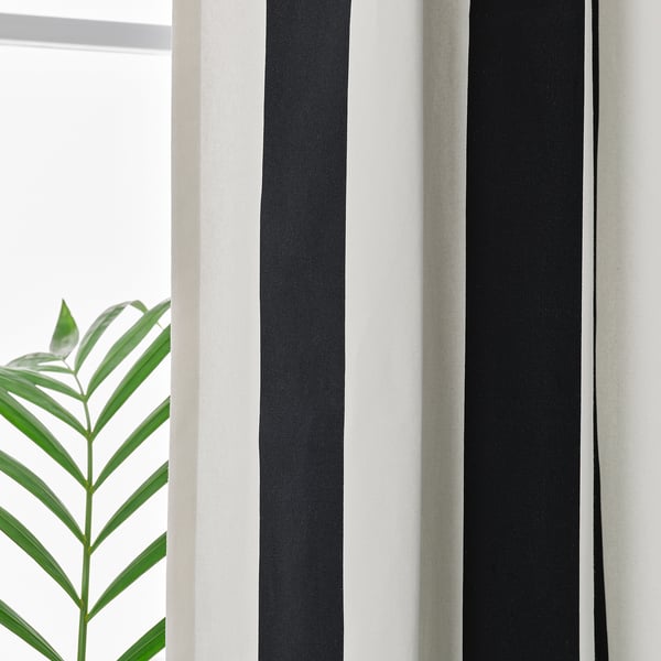 Black and white striped curtains hang, featuring eyelets for easy opening/closing. Green plant leaf visible beside them.