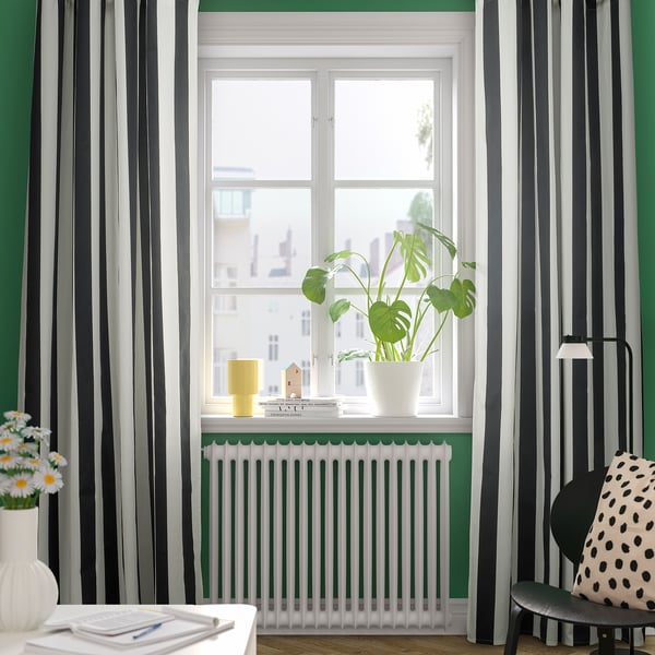 Modern room with green walls, striped curtains, white radiator, plants, and chair with lamp.