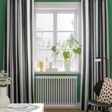 Modern room with green walls, striped curtains, white radiator, plants, and chair with lamp.