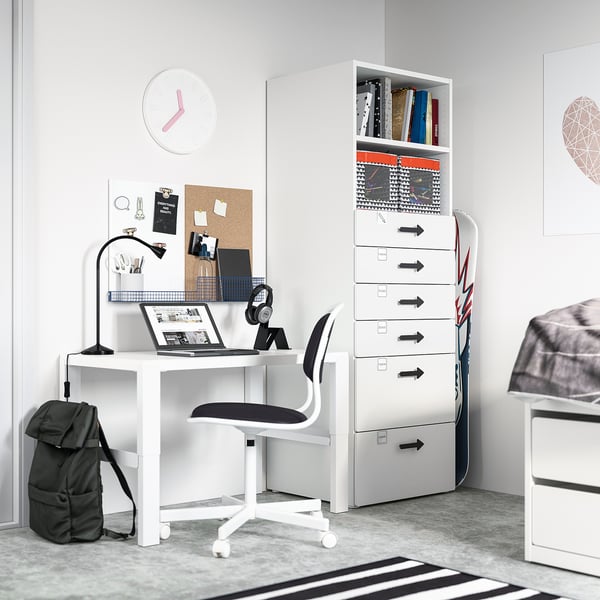 Modern white student desk setup with drawers, chair, and storage. Includes laptop, headphones, and backpack.