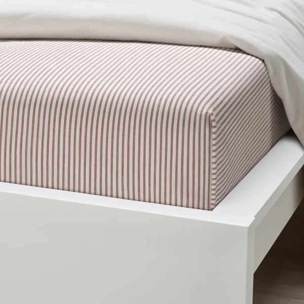 Striped bed sheet on white bed, showcasing soft, recycled cotton quality.