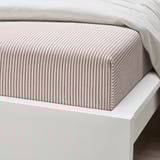 Striped bed sheet on white bed, showcasing soft, recycled cotton quality.