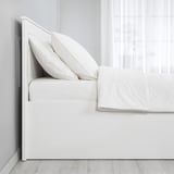 Clean, minimalist bedroom with white SONGESAND ottoman bed, fitted sheet visible.