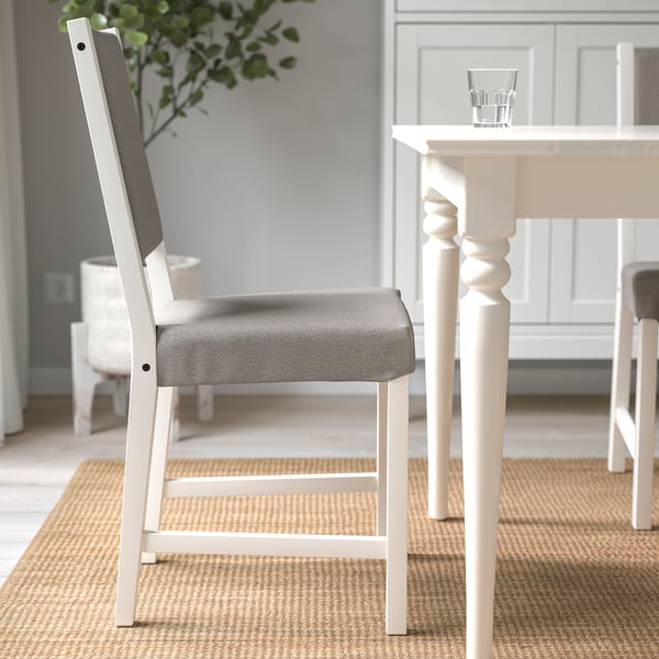 Modern dining set with white chair featuring grey cushioned seat, positioned near a table with a clear glass and plant.