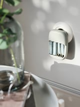 A white STENKOL battery charger with 4 slots hangs on the wall. Modern design, made of recycled plastic.