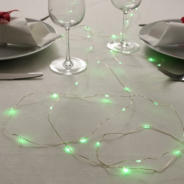 Image a dining setup with illuminated green string lights, wine glasses, plates, and cutlery arranged on a table.