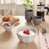 Wooden table set with coffee, pastries, and white ceramic bowls and cups. Bowl in front has yogurt topped with raspberries.