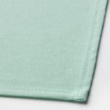 Light green woven cotton napkin, neatly folded. High-quality texture visible.