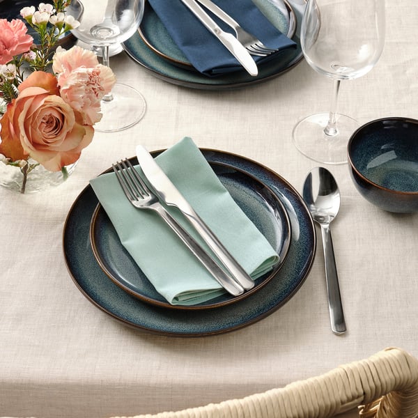 Table set with blue plates, green napkins, and silverware. Wine glasses and flowers enhance the dining experience.