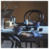 Blue and black ceramic table setting with bread, surrounded by black chairs and light blue napkins.